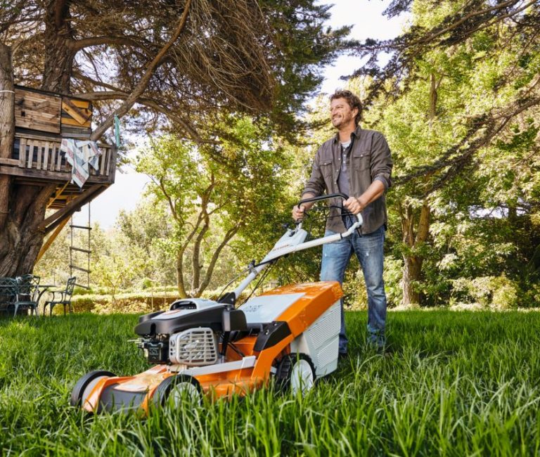 man using his stihl lawn mower to cut long grass under a tree